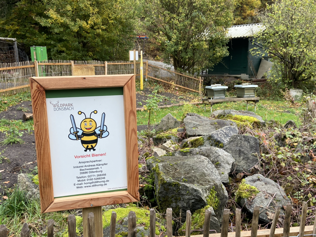 Bienenstand im Wildpark Donsbach mit Holzbeuten und Hinweisschild des Imkers dillhonig.de